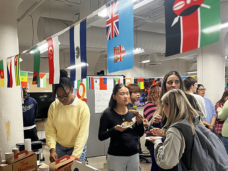 A group of students grabs refreshments with a ribbon of country's flags above them  